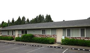 Portland apartment for rent - a gray house with a parking lot and bushes