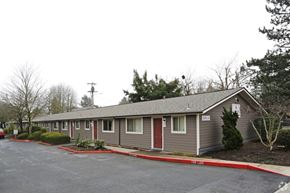 Portland apartment for rent - A building with grey walls and red doors is surrounded by a parking lot.