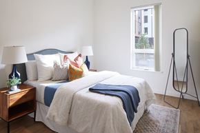 Milwaukie apartment for rent - A bed with a white comforter and a blue blanket is in the center of the room.