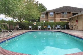 Clackamas apartment for rent - a swimming pool with chairs and a house in the background
