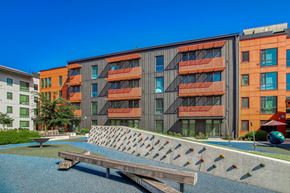 Gresham apartment for rent - A modern building with orange and grey balconies is surrounded by a small pool and a wooden bench.