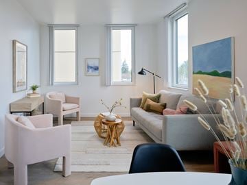 Portland apartment for rent - A living room with a grey couch, a pink chair, and a painting on the wall.
