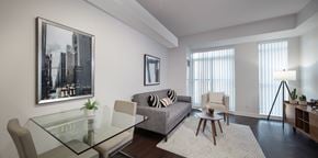 Toronto apartment for rent - A living room with a grey couch, a glass table, a coffee table, a floor lamp, and a large picture on the wall.