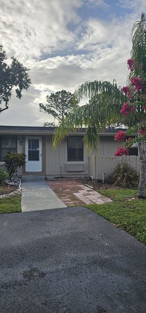 Lakeland apartment for rent - A house with a white door and windows is surrounded by greenery and a paved walkway.