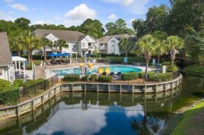 Bluffton apartment for rent - A pool surrounded by a fence and trees with houses in the background.
