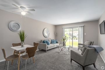 Glassboro apartment for rent - A living room with a grey sofa, a white dining table, and a television on the wall.