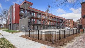Detroit apartment for rent - A modern red and grey building with a black fence in front.