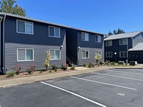 Newberg apartment for rent - A parking lot in front of a grey building with a clear blue sky.