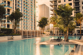 Miami apartment for rent - A swimming pool surrounded by trees and chairs in front of apartment buildings.
