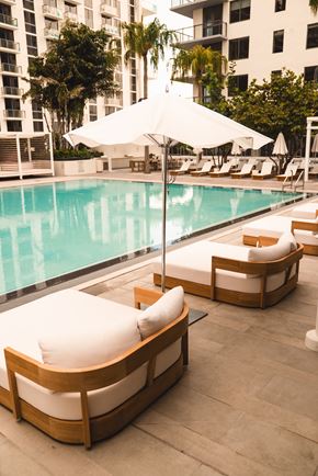 Miami apartment for rent - A poolside lounge area with white cushioned seating and a white umbrella.
