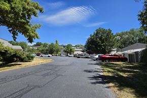 Pocatello apartment for rent - A street with cars parked on the side and trees in the background.