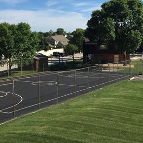 Milwaukee apartment for rent - A basketball court is surrounded by a fence and there are houses in the background.