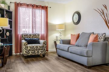 Sacramento apartment for rent - A living room with a grey couch, a patterned chair, and a table with a lamp.