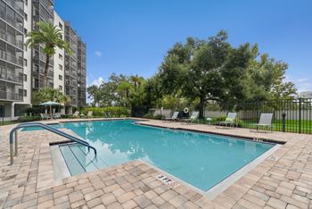 A swimming pool surrounded by a brick patio and lounge chairs.