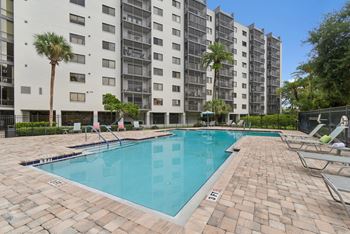 A swimming pool in front of a tall building with palm trees.