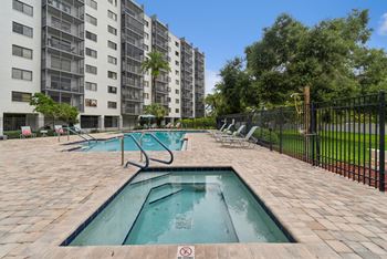 A swimming pool surrounded by a black fence in front of a tall apartment building.