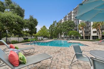 A pool surrounded by chairs and trees with a building in the background.