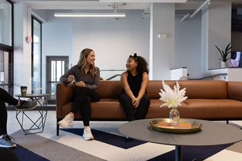 Two women sitting on a couch talking in a lobby