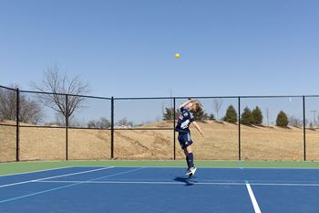 A young boy jumping to hit a tennis ball on a tennis court