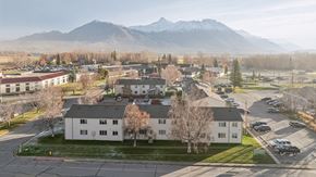 Palmer apartment for rent - A large white building sits in the middle of a parking lot with mountains in the background.
