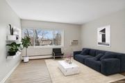 Minneapolis apartment for rent - A living room with a grey sofa, a black chair, a white coffee table, and a window with a view of trees and a building.