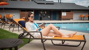 St. Charles apartment for rent - a woman sitting on a chaise lounge by a pool with a tablet in her hand at The Township at St. Charles, Illinois, 60174