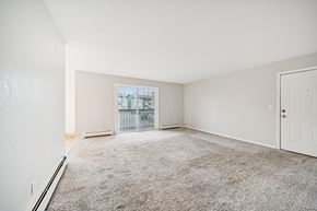 Eagle River apartment for rent - A spacious room with a carpeted floor and a view of a balcony through a window.