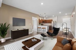 Pittsburgh apartment for rent - A modern living room with a brown sofa, a wooden coffee table, and a flat-screen TV mounted on the wall.