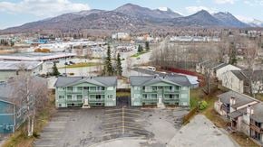 Eagle River apartment for rent - A parking lot with two green buildings in the foreground and mountains in the background.