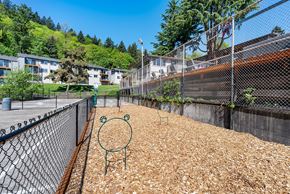 Portland apartment for rent - A playground with a green monkey swing set sits in the middle of a wood chip area.