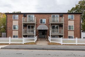 Worcester apartment for rent - the front of a brick apartment building with a white fence at Flats at Merrill Pond, Massachusetts