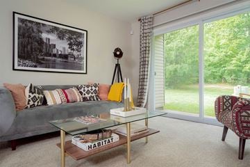 Farmington Hills apartment for rent - A living room with a grey couch, a glass coffee table, and a chair with a patterned cushion.