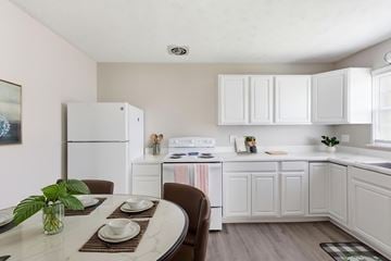 Winchester townhouse for rent - A kitchen with white appliances and cabinets, a dining table set with plates and a potted plant on it.