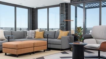 Minneapolis apartment for rent - A living room with a grey couch, a brown ottoman, and a black table with a plant on it.