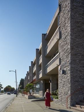 Vancouver apartment for rent - A woman in a red dress is walking down a sidewalk next to a stone building.