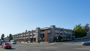 Vancouver apartment for rent - A red car is driving on a street past apartment buildings.