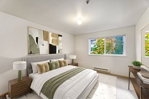 Puyallup apartment for rent - A bedroom with a large bed and a window showing trees outside.