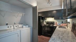 Duluth apartment for rent - Duluth, GA Townhomes - Amberlake Village - Laundry Closet With Full Sized Washer And Dryer Beside Modern Kitchen With Dark Cabinets And Granite Countertops.