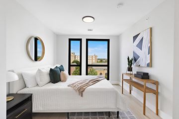 Newark apartment for rent - A bedroom with a large bed, a mirror, a window with a view, and a wooden nightstand.