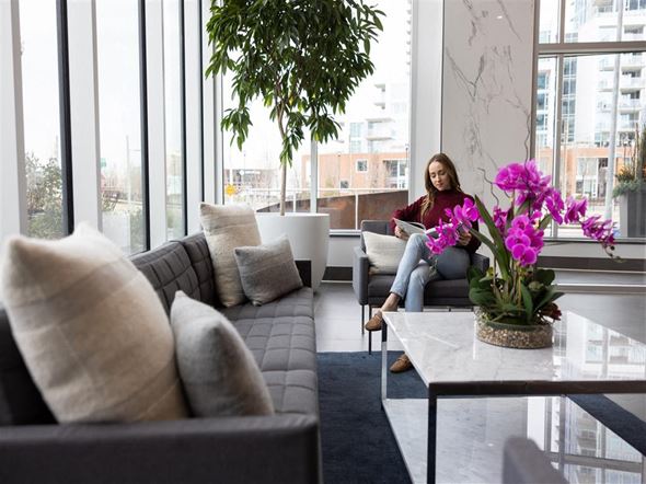 Calgary apartment for rent - a woman sits on a couch in a living room with large windows