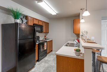 Spokane Valley apartment for rent - A black refrigerator stands in a kitchen with wooden cabinets and a white countertop.