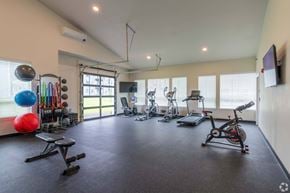 Spokane apartment for rent - A spacious home gym with various exercise equipment and a television mounted on the wall.