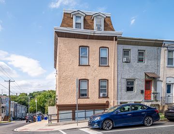 Philadelphia apartment for rent - A blue car is parked in front of a tan building.
