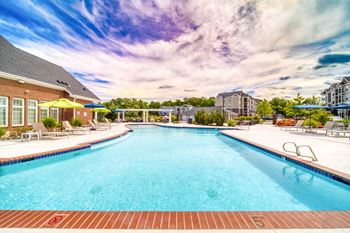 A swimming pool with lounge chairs and umbrellas in front of a brick building