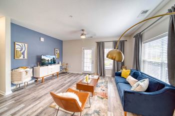 A living room with a blue couch and chairs and a flat screen tv on the wall