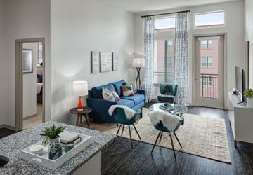 Denver apartment for rent - A living room with a blue couch, a chair, and a table with a plant on it.