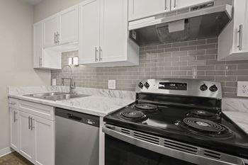 A kitchen with a stove, sink, and cabinets.
