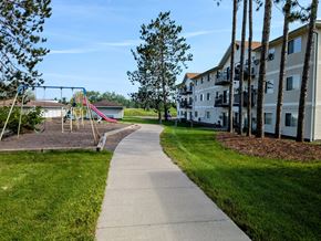 Cloquet apartment for rent - A playground with a slide and swings is surrounded by a grassy area and a sidewalk.