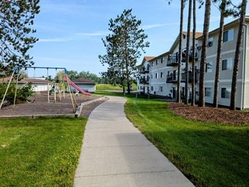 Cloquet apartment for rent - A playground with a slide and swings is surrounded by a grassy area and a sidewalk.