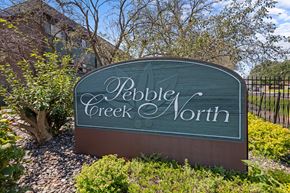 Brooklyn Park apartment for rent - A sign that says Pebble Creek North is shown in front of a fence and some trees.
